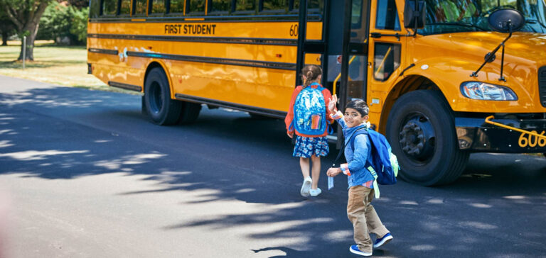 A child waving while getting on a school bus.