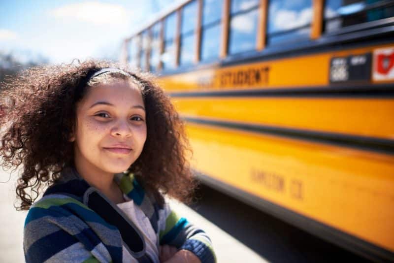 student in front of yellow school bus