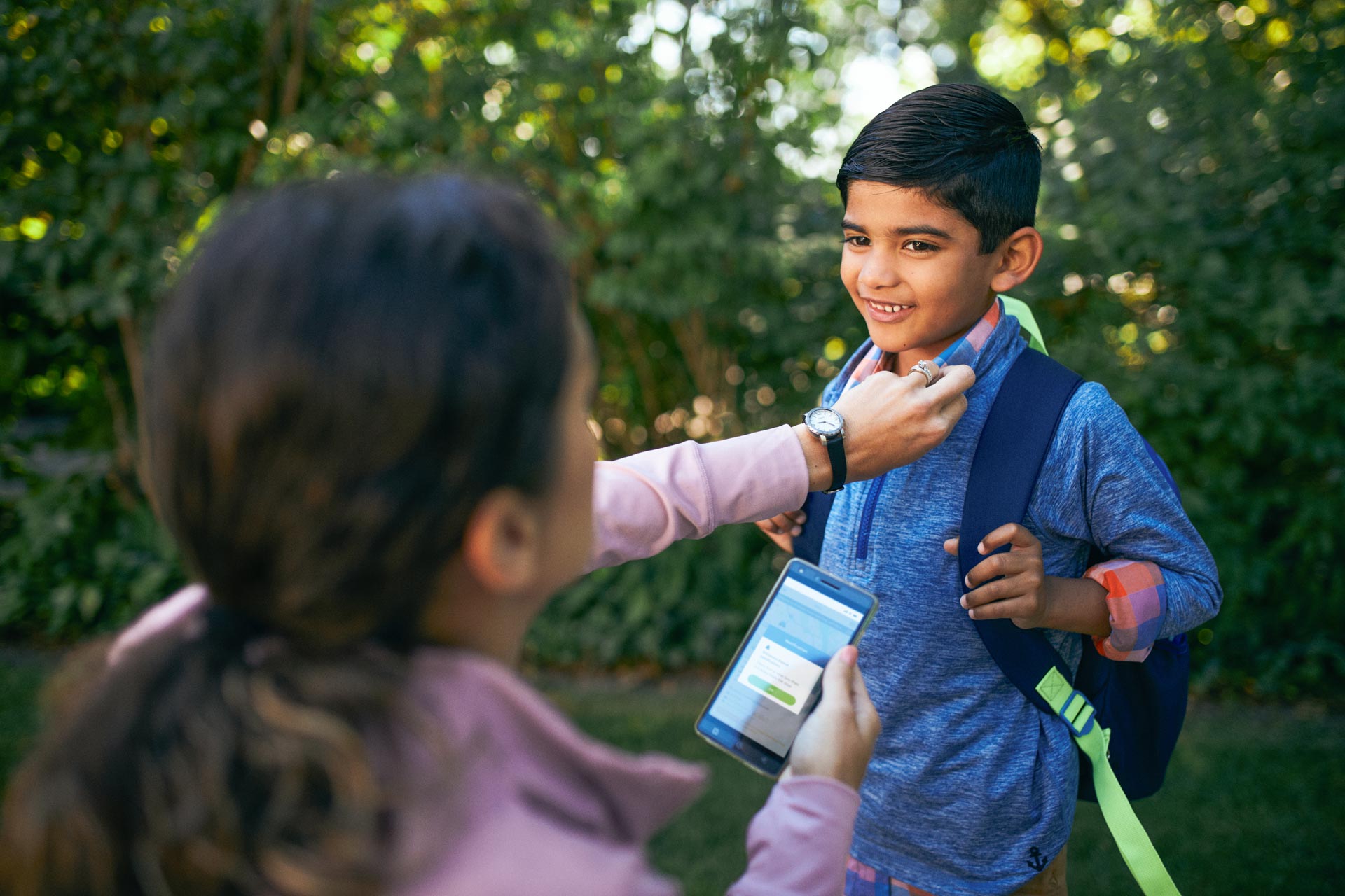 A mother looking at the First Student Halo app while her child looks at her.