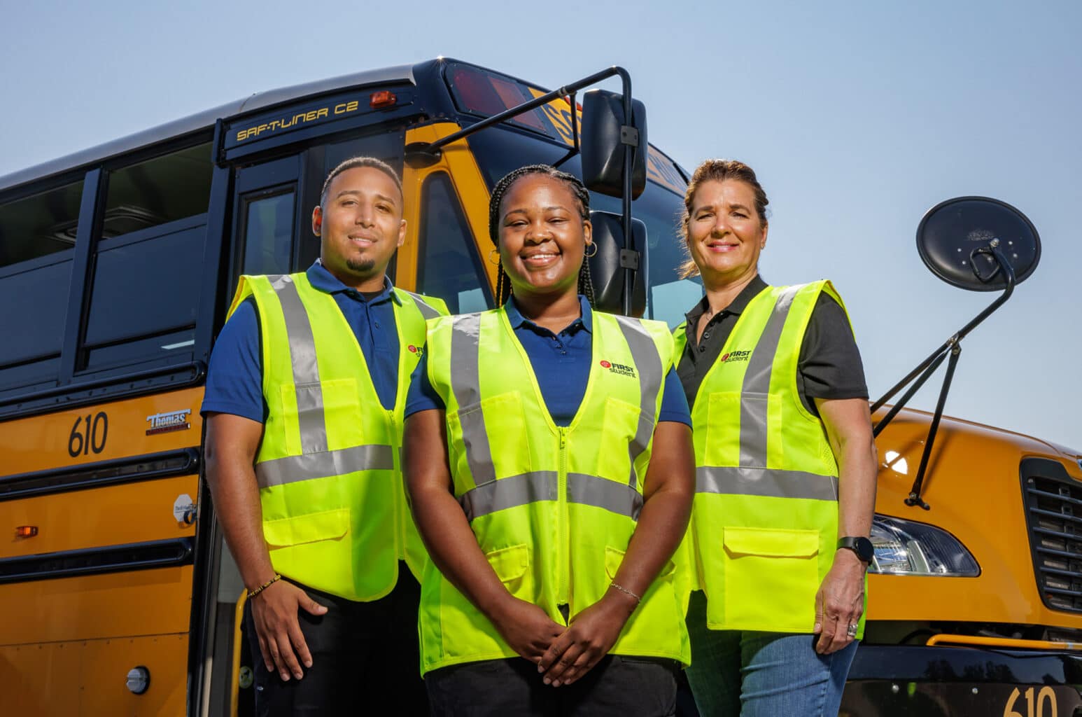 Three bus drivers in safety vests in front of school bus